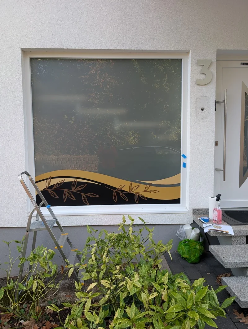 Montageschritt: Das gold-schwarze Blattdekor ist am unteren Fensterrand angebracht
